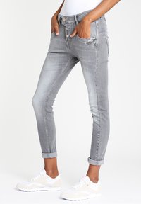 Slanke grijze jeans met een versleten ontwerp, voorzien van een hoge taille, vijf zakken, opgerolde mouwen en metallic knopen, gecombineerd met witte sneakers.