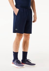 Navy blue athletic shorts in lightweight material, featuring an elastic waistband and side pockets; Lacoste logo in green on left leg.