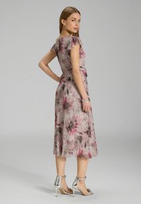 Robe à imprimé floral en tissu doux avec fronces aux épaules, tons pastel de rose et de gris, longueur midi fluide, associée à des talons à bride cheville en argent.