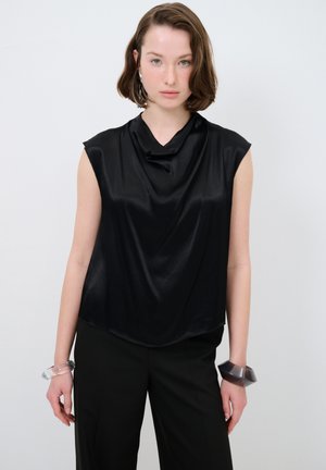 Top senza maniche in satin nero con scollatura drappeggiata, texture liscia, abbinato a pantaloni neri e bracciali trasparenti.