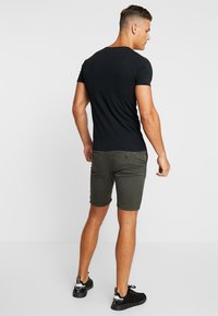 Camiseta de algodón negra de manga corta combinada con pantalones cortos verde olivo que cuentan con un bolsillo trasero, el usuario está de espaldas y lleva zapatillas negras.