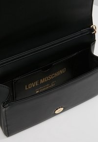 Svart läderhandväska med ett guldknäppstängning. Inuti finns ett fack och en kortplats märkt "LOVE MOSCHINO." Slät textur.