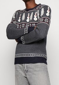 Maglione lavorato a maglia blu navy con motivi di pupazzi di neve e alberi di pino in bianco e rosso, con maniche strutturate e orlo a coste.