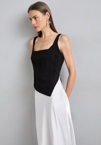 Black sleeveless top with a square neckline, structured design, and a pointed hem, paired with a flowing white skirt.