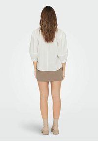 Weiße Bluse mit Volantsärmeln und Rückenfalte; kombiniert mit einem beigen Minirock und taupefarbenen Stiefeletten, von hinten betrachtet.