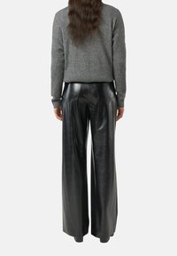 Szary sweter z dzianiny i czarne szerokie spodnie z ekologicznej skóry, oba o gładkiej fakturze. Sweter ma prążkowane mankiety i dół.