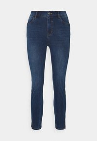 Jeans ajustados de color azul oscuro con bolsillos frontales, cierre de botón y cremalleras en los tobillos sobre un fondo blanco.