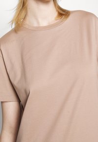 T-shirt à manches courtes, col rond en coton beige clair. Texture douce avec des coutures minimales, mettant en avant une coupe décontractée.