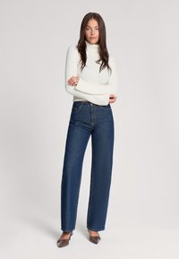 Jeans in denim blu a vita alta con un design a gamba larga, dotati di un classico stile a cinque tasche e dettagli di cucitura sottili.