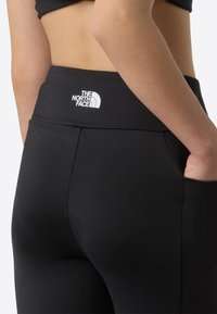 Čierne legíny s vysokým pásom a bielym logom "The North Face." Vyrobené z elastickej látky s bočnými vreckami.