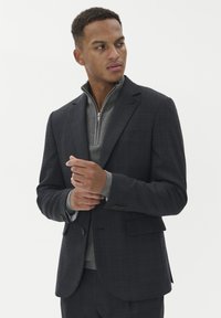 Ciemnoszary żakiet z delikatnym wzorem w kratkę, dopasowany fason i zapięcie na dwa guziki, nałożony na jasnoszary sweter z podwyższonym kołnierzem.