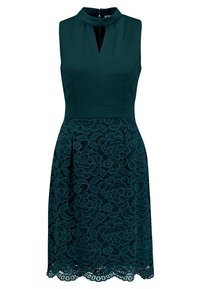 Dunkelblaues Kleid mit hohem Ausschnitt, Schlüssel-Loch-Detail und einer Spitzenüberlage mit floralen Mustern. Ein gewellter Saum vollendet das Design.
