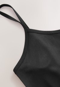 Canotta nera con spalline sottili, tessuto dalla texture liscia e bordi cuciti. Presenta un design semplice e aderente senza motivi visibili.