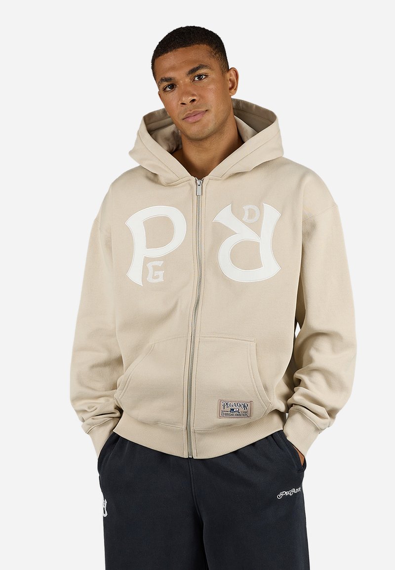Beige zip-up hette med store hvite logobokstaver foran, kengurulomme og ribbestrikkede mansjetter. Laget av myk stoff med en avslappet passform.