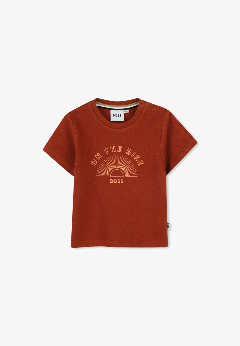 T-shirt à manches courtes couleur rouille avec col rond, comportant un texte à l'avant "ON THE RISE" et un graphisme de soleil. Boutons-pression à l'épaule.