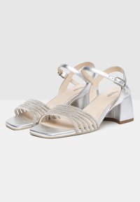 Sandales à talon bloc argentées, avec des brides croisées ornées de strass et un design à bout carré.