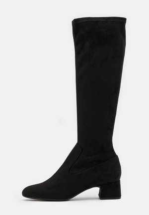 Botte noire montante pour femme, avec talon bloc bas et surface lisse, non ornée, vue de profil sur fond blanc.