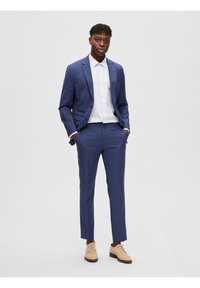 Blau kariertes Anzug mit taillierter Passform, kombiniert mit einem weißen Hemd und beigen Schuhen. Der Anzug verfügt über gerade geschnittene Hosen und Reverskragen.