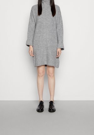 Abito maglione grigio a coste con collo alto e maniche lunghe, caratterizzato da una vestibilità ampia e spacco laterale, abbinato a scarpe nere.