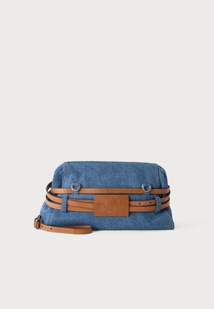 Denim clutch taske med dobbelt brun læderbælte og matchende læderlogo på midten mod en ensfarvet baggrund.