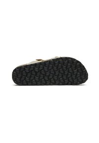 Light beige shoe with a textured black rubber sole featuring circular patterns and a tan strap detail on the upper.