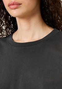 Tumehall sweatširti ümar kael ja soonikkoes. Sile tekstuur ja vähene õmblusdetail, mis on nähtav kaela piirkonnas.