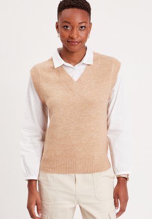 Chaleco de punto color marrón claro con escote en V y dobladillo acanalado, superpuesto a una camisa blanca con cuello, con textura suave y diseño ajustado.
