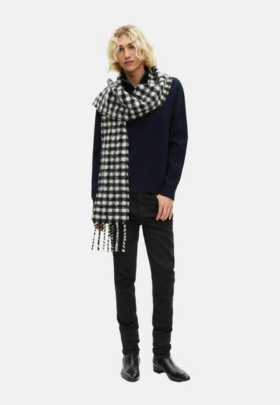 Czarny i biały w kratkę szalik z frędzlami zarzucony na szyję, zestawiony z granatowym swetrem i czarnymi dżinsami, noszony z czarnymi botkami.