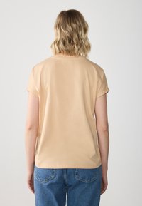 Kortærmet, ferskenfarvet t-shirt i blød kvalitet, med rund hals og en afslappet pasform, sammen med blå denim jeans.