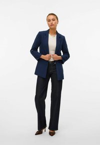 Navy blazer with a structured design, single button closure, and long sleeves, paired with dark denim jeans and pointed-toe heels.