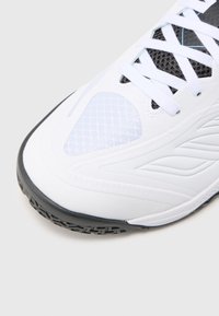 Białe sportowe sneakersy z teksturowaną siatką, czarną gumową podeszwą i gładką syntetyczną cholewką. Posiadają białe sznurówki i wzorzyste akcenty.