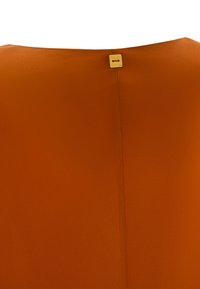 Indumento arancione con una texture liscia. Presenta un collo arrotondato e un piccolo etichetta dorata sul retro. Mostra una linea di cucitura pulita.