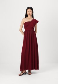 Rochie maxi burgundy cu un umăr, cu un corset din dantelă texturată, fustă din chiffon fluid și talie ajustată. Sandale negre cu bretele completează ținuta.