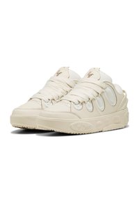 Gräddfärgade sneakers med rundad design, texturerat läder och elastiska snören. Har mönstrade detaljer på sidorna och en tjock sula.