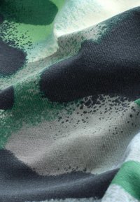 Tekstil med et camouflage mønster i nuancer af grønt, sort og beige. Stofoverfladen virker blød, tekstureret og let krøllet.