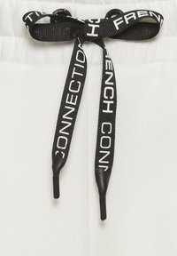 Weiße Jogginghosen mit einem schwarzen Kordelzug und "FRENCH CONNECTION"-Branding, glatter Textur und elastischem Bund.