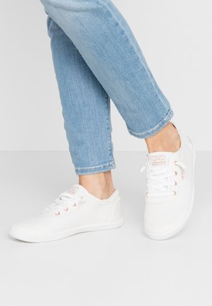 White canvas sneakers with a low-top design, featuring rose gold eyelets and a textured edge. Paired with light blue jeans.