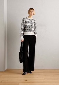 Maglione a maglia con motivo in bianco e nero, con polsini a coste, abbinato a pantaloni larghi neri e tacchi a spillo, mentre tiene una borsa a righe.