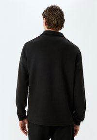 Pull della felpa nera in pile con colletto, maniche lunghe e polsini a coste. Texture morbida, progettata per comfort e calore.