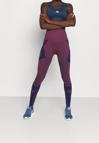 Soutien-gorge de sport marine et leggings bordeaux avec des accents géométriques marins ; les leggings présentent une taille haute et des détails rayés. Chaussures de sport bleues.