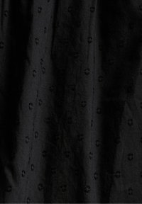 Tissu noir avec un motif texturé de petits motifs circulaires en relief uniformément répartis sur la surface, créant un design subtil.