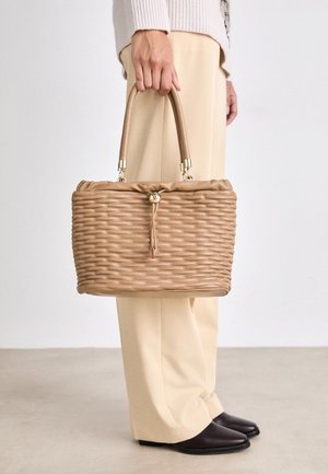 Vævet tan håndtaske med rund form, samlet top og en guldtoggle-lukning. Har to beige håndtag. Glat tekstur, enkelt design.