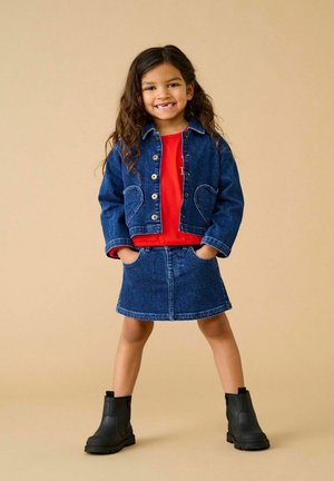 Denim jakna s žepom v obliki srca, rdeča majica, denim krilo in črne gležnjarje. Postavljeno na nevtralno ozadje.