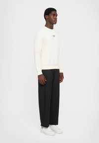 Sudadera crema con el logo de EA7, combinada con pantalones negros holgados y zapatillas blancas. Tejido suave, detalles de puños y cinturilla acanalados.
