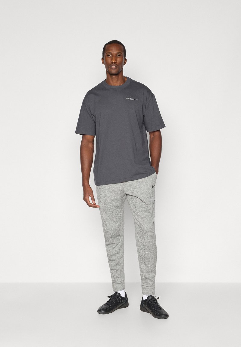Gray t-shirt with short sleeves, “BARCA” print, paired with light gray sweatpants and black athletic shoes. Simple, casual design.
