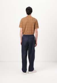 Brun skjorta med diamantmönster och kort ärm, tillsammans med marinblå vida byxor som har elastisk midja och en slät textur.