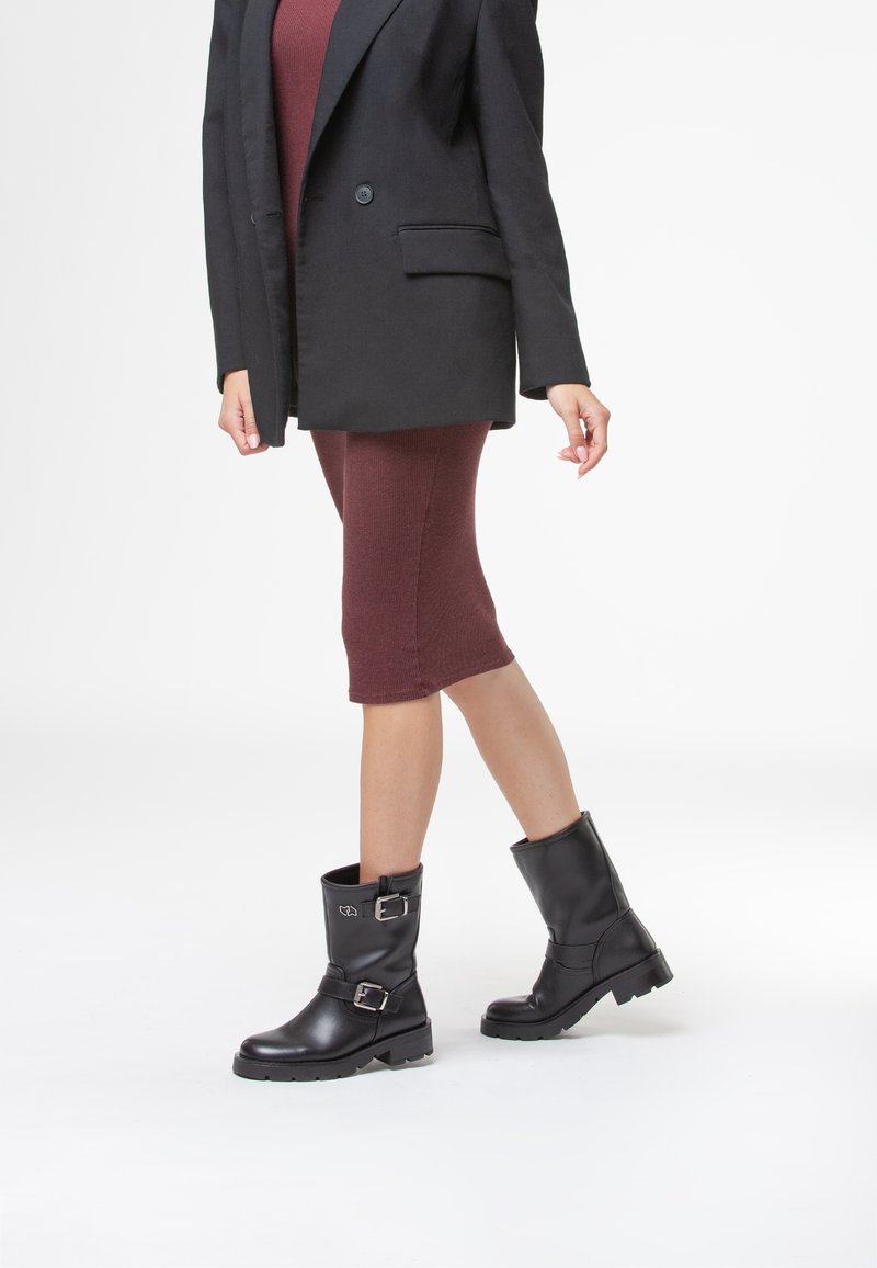 Stivaletti neri in pelle con punta arrotondata, fibbie laterali e suola in gomma testurizzata. Indossati con un abito fitted bordeaux e un blazer.
