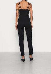Czarny kombinezon z cienkimi ramiączkami, dopasowanym gorsetem i zwężanymi nogawkami. Materiał wygląda na gładki, z dyskretnym zapięciem na zamek z tyłu.