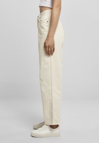 Beige wijde jeans van textiel met een hoge taille, voorzien van zij- en achterzakken, gedragen met witte sneakers.