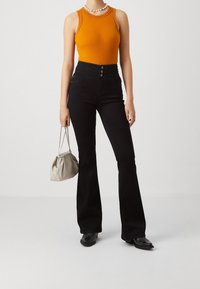 Svarta utsvängda byxor med hög midja och knappstängning, kombinerade med en ljus orange ribbad linne med texturerade detaljer.